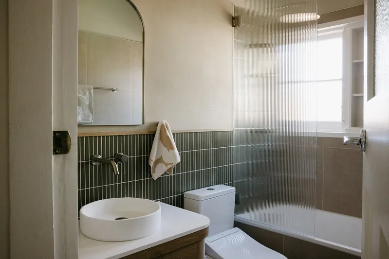 The completed main bathroom, with green wall tiles, timber vanity and retained bathtub
