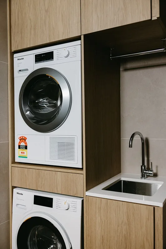 Stacked washer and dryer beside laundry sink and timber storage